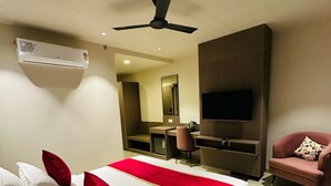 Ein modernes Hotelzimmer mit einem großen Bett, einem Deckenventilator, einem Flachbildfernseher, einer Sitzecke mit einem Sessel und einem kleinen Schreibtisch.