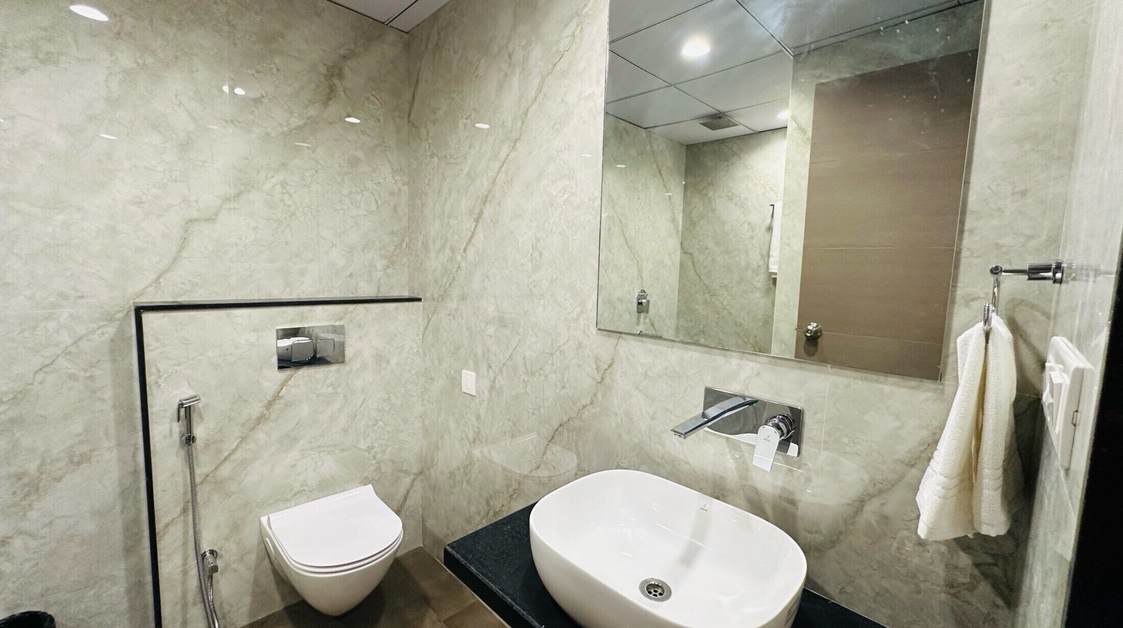 Een moderne badkamer met een marmeren vloer, een wit toilet, een wastafel en een spiegel.