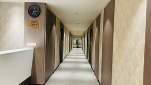 Ein Hotelgang mit einer Uhr, Check-in- und Check-out-Zeiten sowie einer Pflanze in der Mitte.