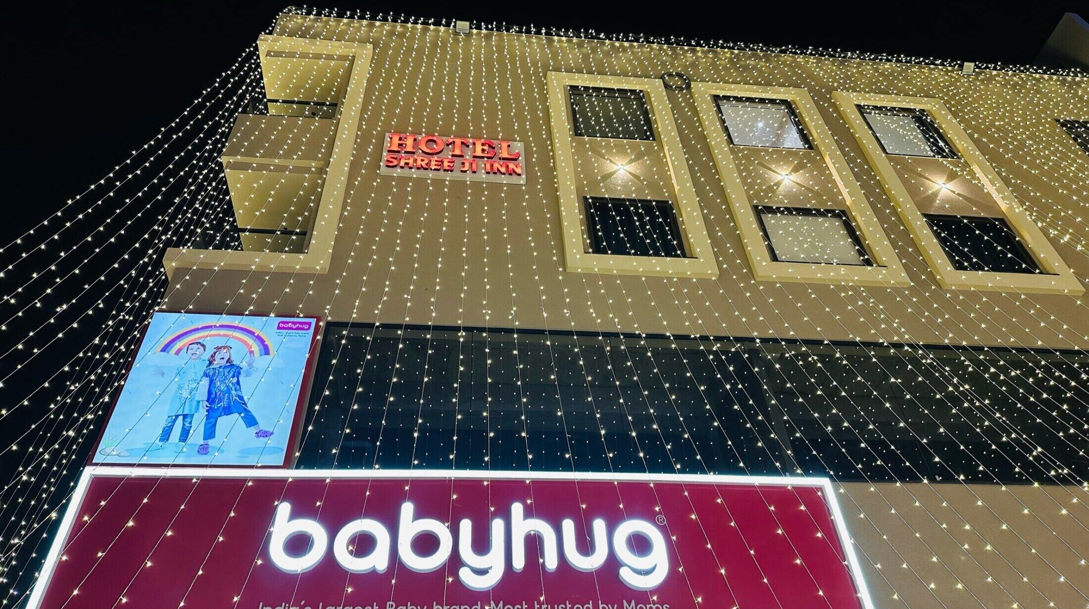 A hotel facade with string lights and signage for 'HOTEL SHREEJI INN' and 'babyhug'.