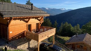 Une cabane en bois dotée d’un balcon, construite sur des fondations en pierre et offrant une vue sur les montagnes.