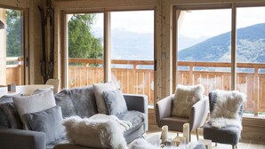 A cozy room with a wooden ceiling, large windows offering mountain views, a sofa set, and a chair. - Luxury Chalet With Sauna and Garden (Vex)