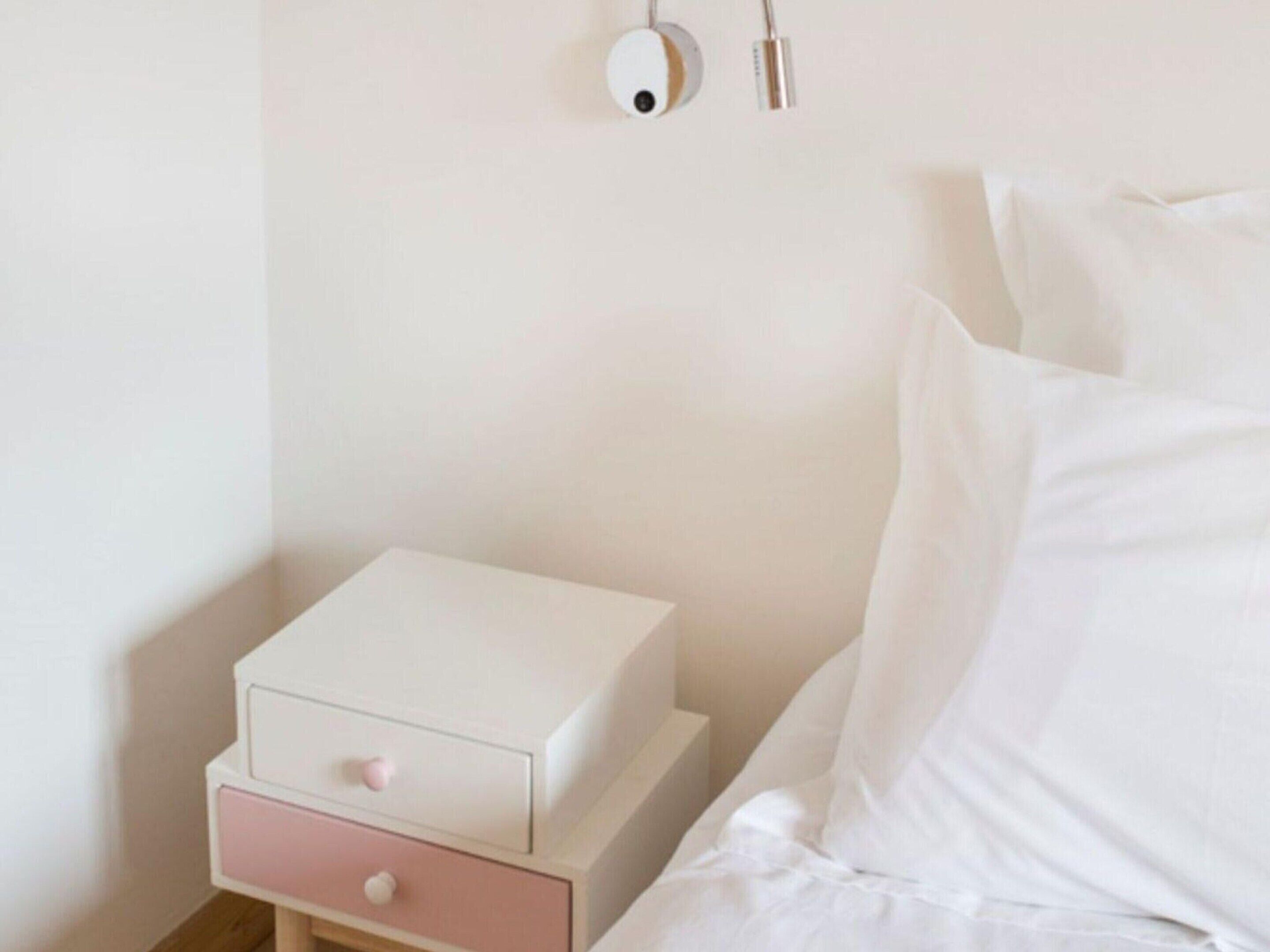 A neatly made bed with white linens, a small bedside table with a drawer, and a wall-mounted light fixture.