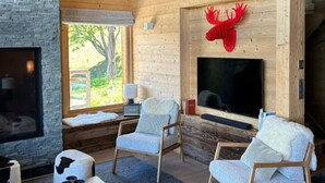 Un salon chaleureux avec une cheminée, des fauteuils confortables et un grand écran de télévision.