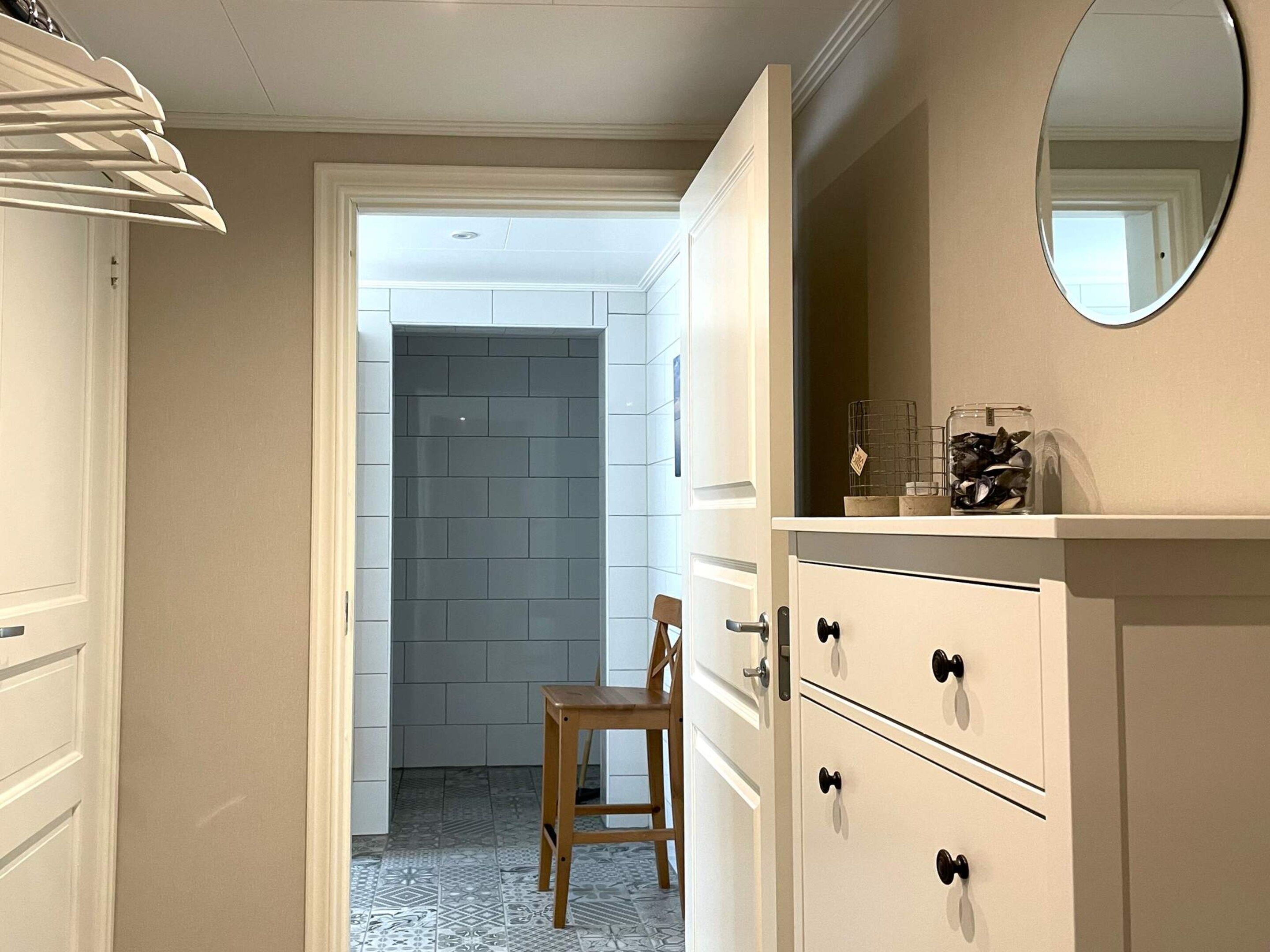 Un couloir avec une armoire blanche, une chaise en bois et un miroir accroché au mur.