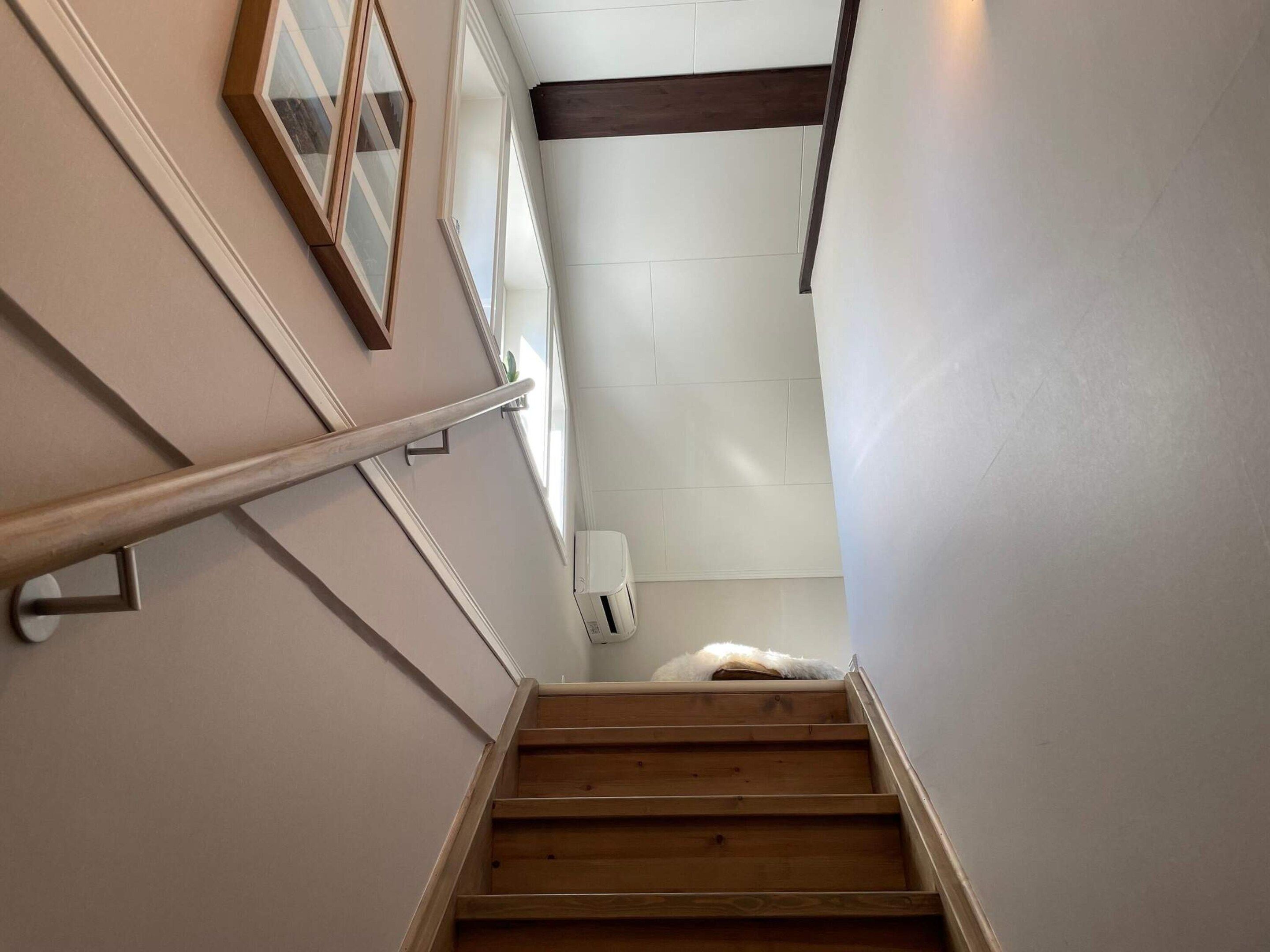 A wooden staircase with a handrail, white walls, and a ceiling with a dark beam.