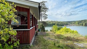 A red cabin with a porch overlooking a lake, surrounded by greenery and trees. - 4 Star Holiday Home in Valdemarsvik (Valdemarsvik)