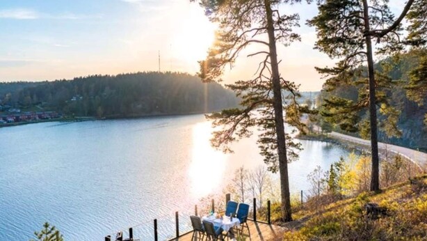 A lakeside dining area with a table and chairs, surrounded by trees and a view of the lake. - 4 Star Holiday Home in Valdemarsvik (Valdemarsvik)