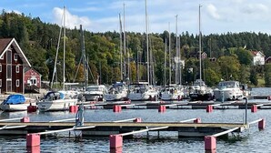 A marina with multiple boats docked at wooden piers, surrounded by residential buildings and a forested hillside. - 4 Star Holiday Home in Valdemarsvik (Valdemarsvik)