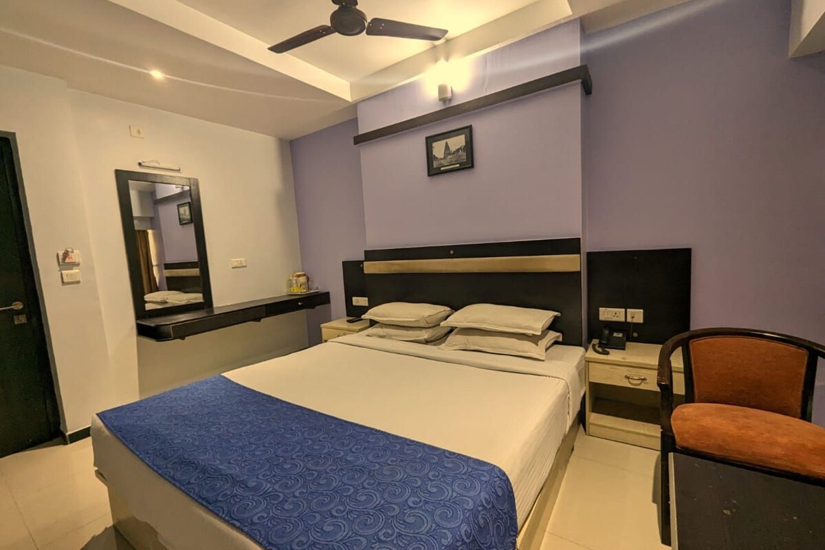 A hotel room with a bed, a chair, a nightstand, a desk, a mirror, and a ceiling fan.