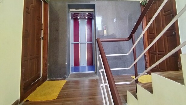 A hallway with wooden doors, a yellow mat, and a staircase with metal railings. - CTS Residency (Tiruchirappalli)