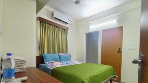A hotel room with a bed, a wooden desk, an air conditioner, a water bottle, and a folded towel. - CTS Residency (Tiruchirappalli)