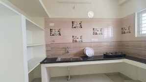A kitchen with a black countertop, a sink, a gas stove, and decorative wall shelves. - CTS Residency (Tiruchirappalli)