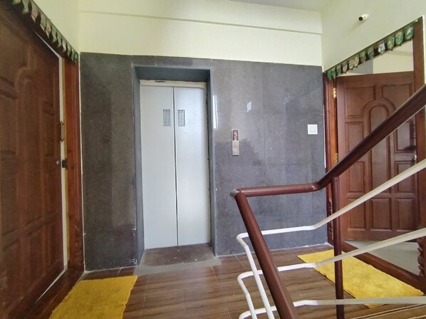 An interior hallway with a wooden door, a white elevator, and a yellow rug on the floor. - CTS Residency (Tiruchirappalli)