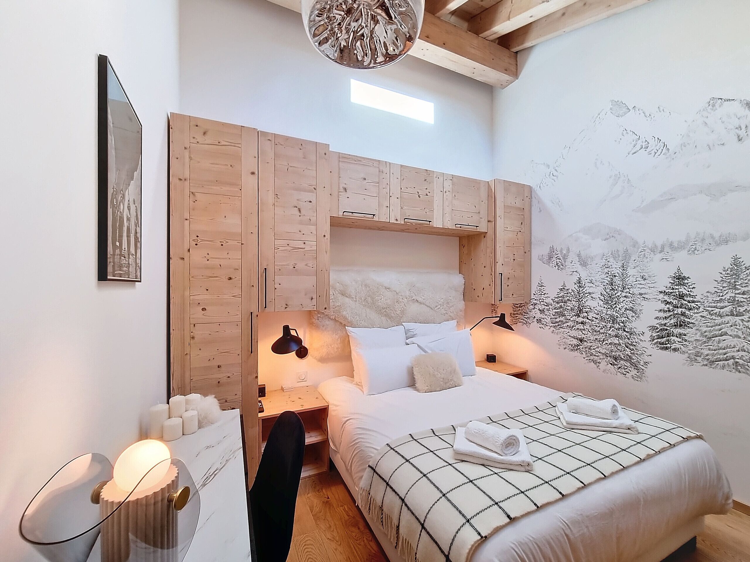Un dormitorio con cama, cabecero de madera, decoración en la pared y una mesita de noche con lámpara.