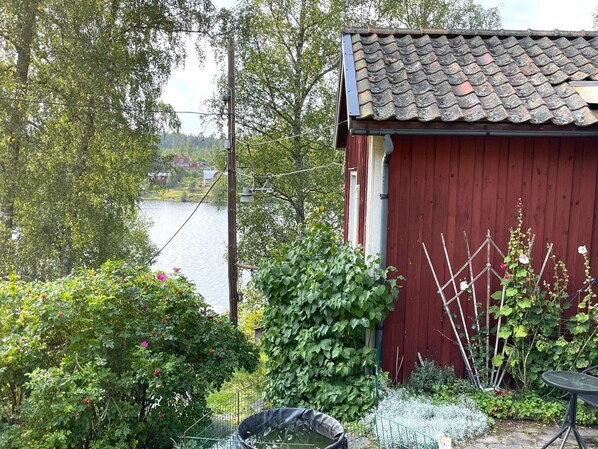 Un edificio in legno rosso con tetto a tegole, immerso nel verde e con vista su un lago.