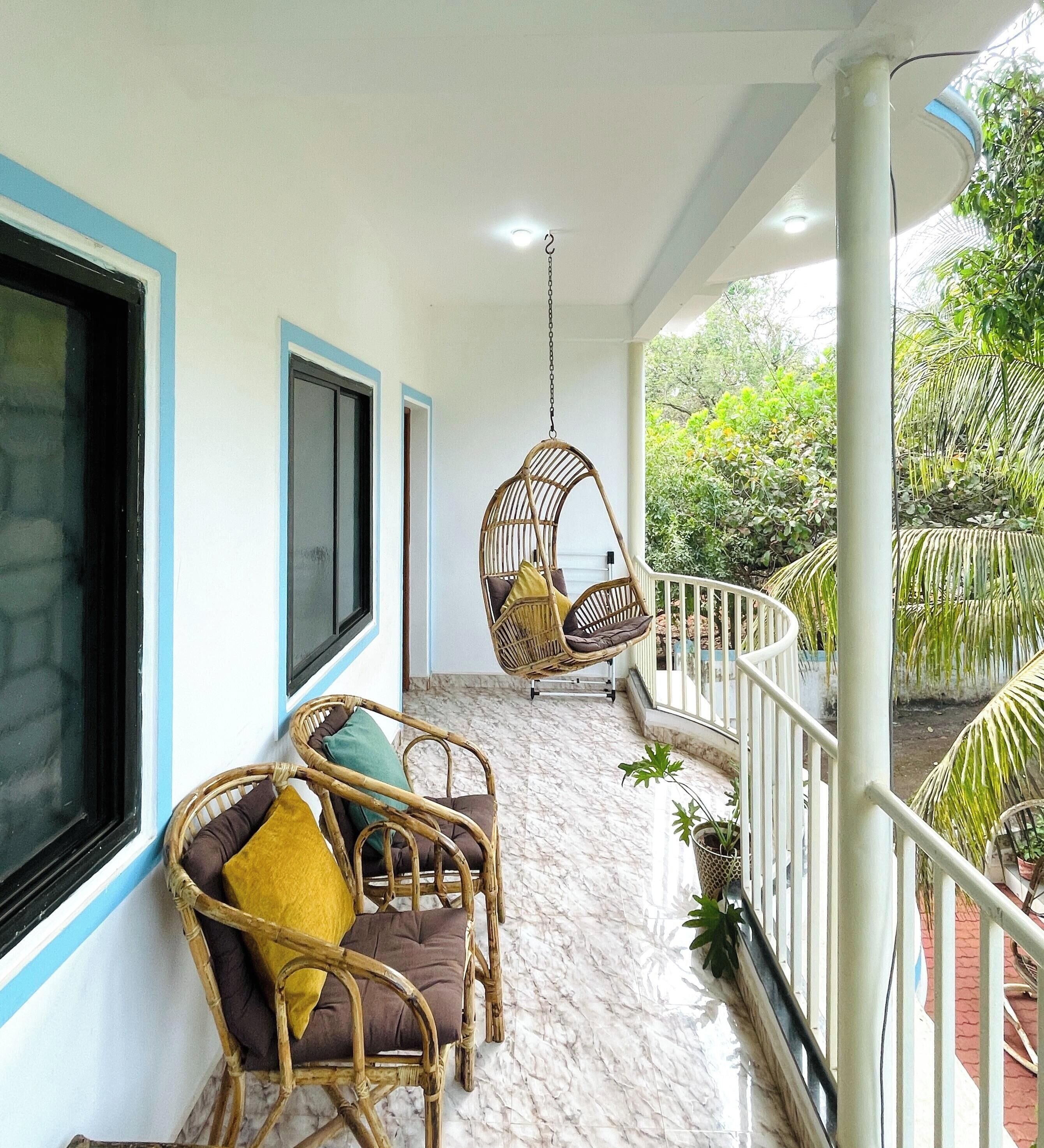 A balcony with wicker chairs and a hanging chair, a potted plant, and a view of greenery.