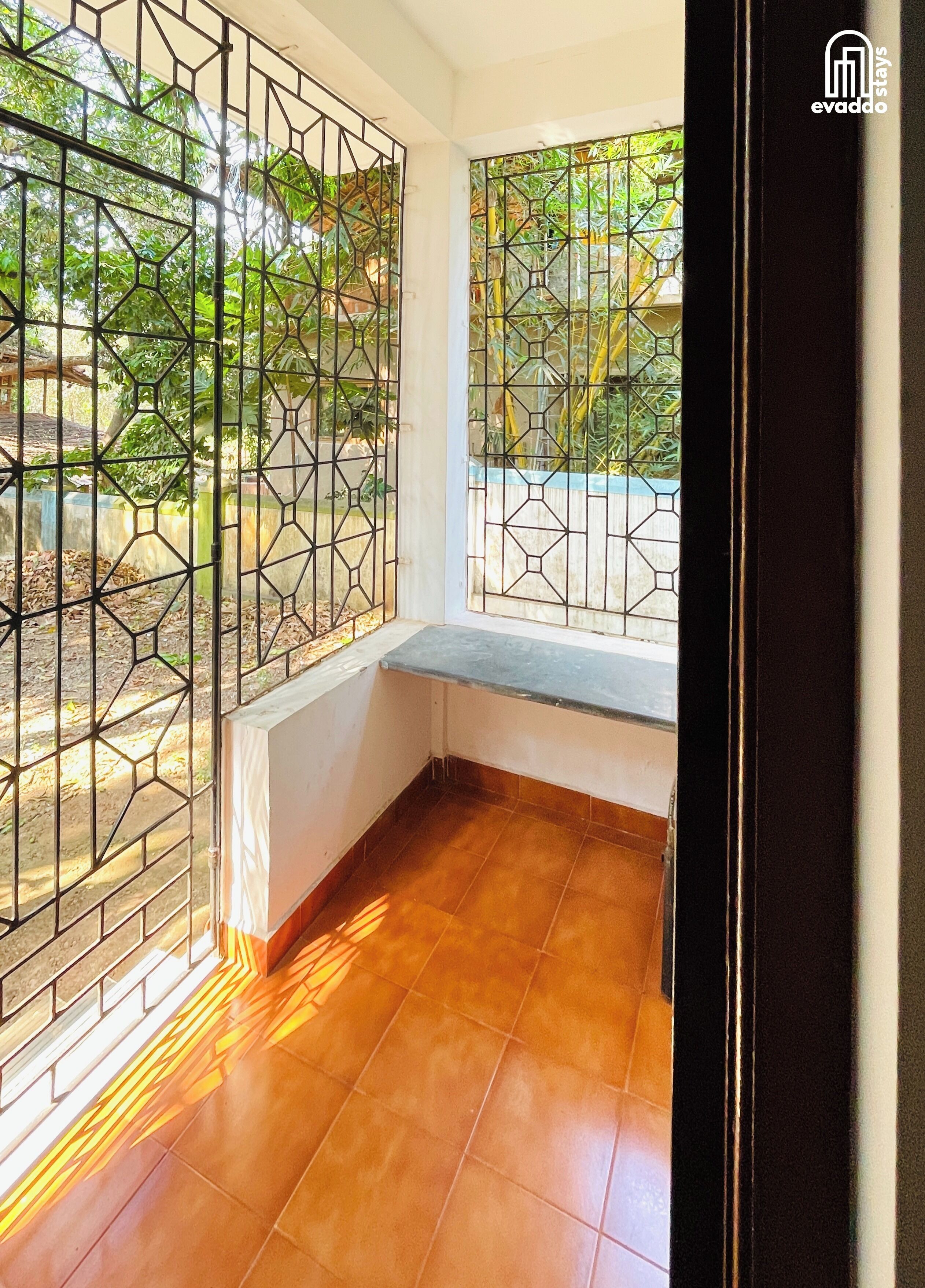 A corner room with a bench, a tiled floor, and a view through a barred window.