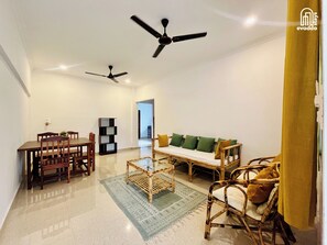 A spacious living area with a dining table, chairs, a sofa with cushions, a coffee table, and two ceiling fans. - Aamra ghar by evaddo stays (Mandrem)