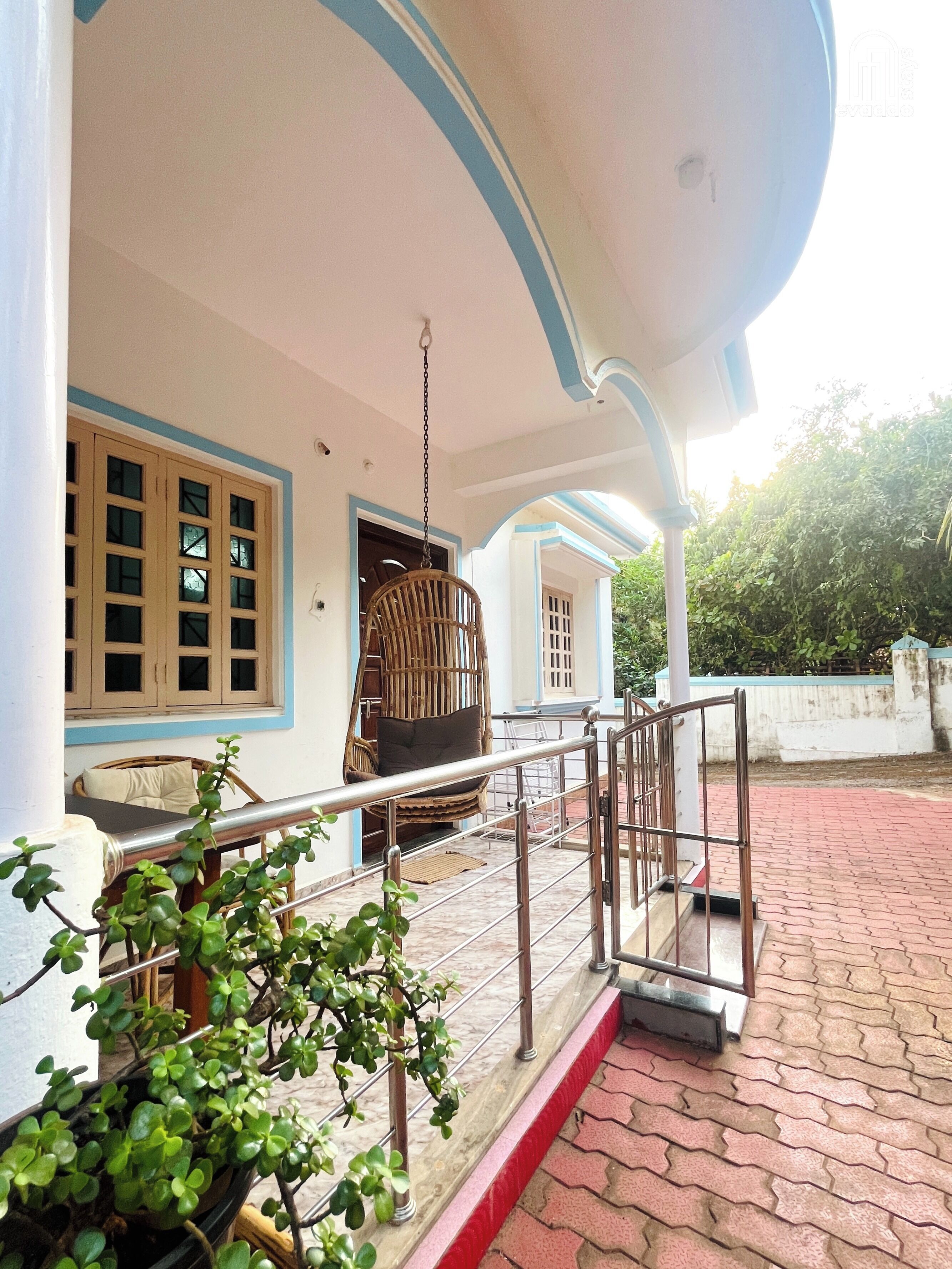 A building with a porch, a hanging chair, and a potted plant.