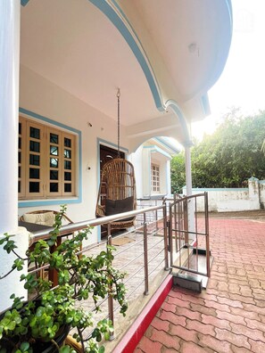 A building with a porch, a hanging chair, and a potted plant. - Aamra ghar by evaddo stays (Mandrem)