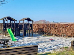 A wooden play structure with a slide and a fenced area with a vineyard in the background. - 5 Star Holiday Home in Faaborg (Faaborg)