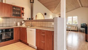 Une cuisine moderne avec des meubles en bois, un lave-vaisselle et une cuisinière. Une grande fenêtre se trouve dans le salon attenant.