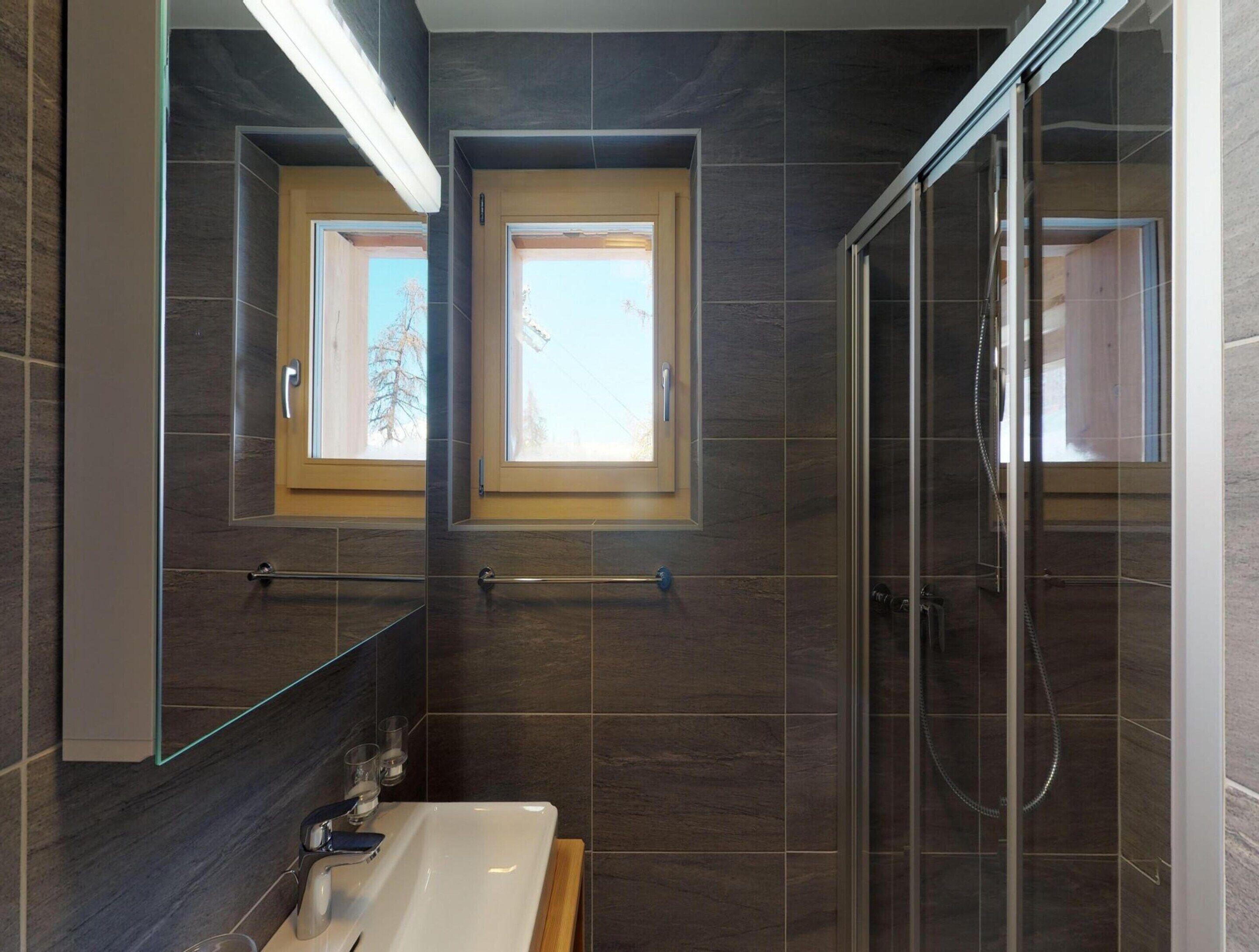 Un baño moderno con ducha envuelta en vidrio, un espejo grande y un ventanal sobre el lavabo.