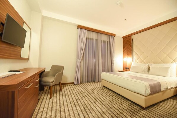 A hotel room with a bed, a desk with drawers, a chair, a television mounted on the wall, and a window with curtains. - Hotel Union (Podgorica)