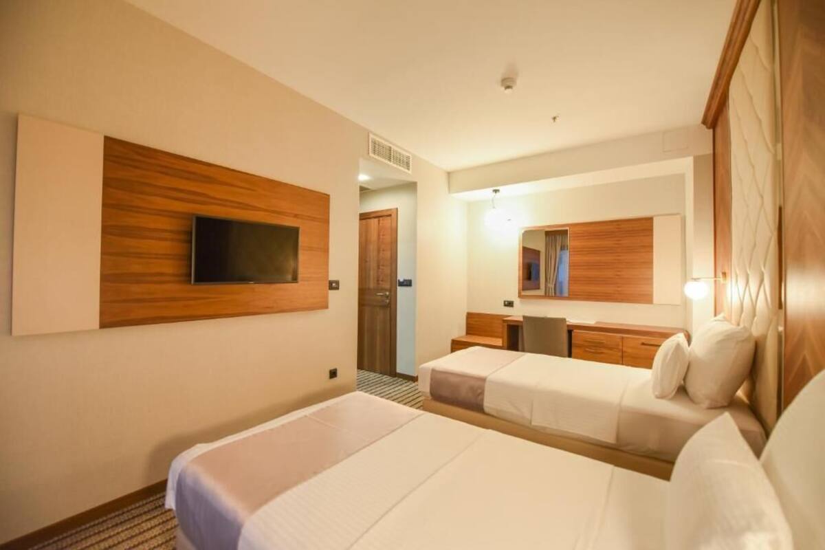 A hotel room with two beds, a TV mounted on the wall, a mirror, and a wooden headboard.