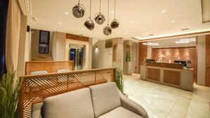 Eine Hotlellobby mit einer Rezeption, einer Wartezone inklusive Sofa und einer Holzwand.