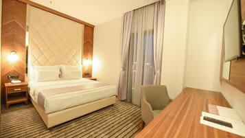 A hotel room with a large bed, a wooden headboard, a desk with a chair, and a large mirror on the wall.