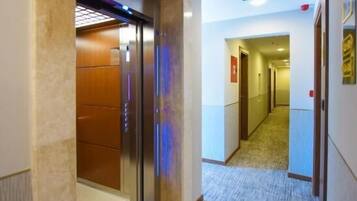 A hotel hallway with an elevator, carpeted floor, and a fire exit sign.