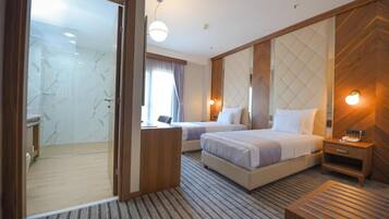 A hotel room with a large bed, a smaller bed, a desk, and a shower area.