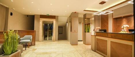 A hotel reception area with a modern design, featuring a reception desk, seating area, and a geometric patterned floor.