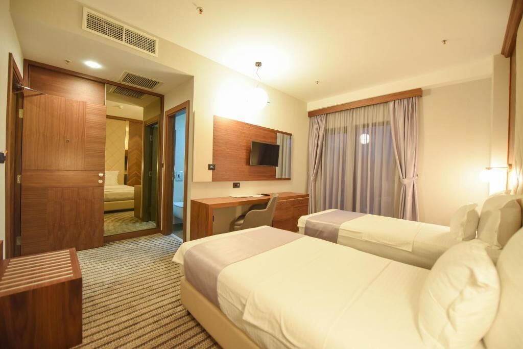 A hotel room with two beds, a desk, a chair, a TV, and a wardrobe.