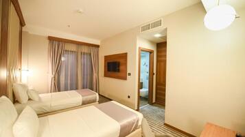 A hotel room with two beds, a TV mounted on the wall, and a bathroom visible through an open door.