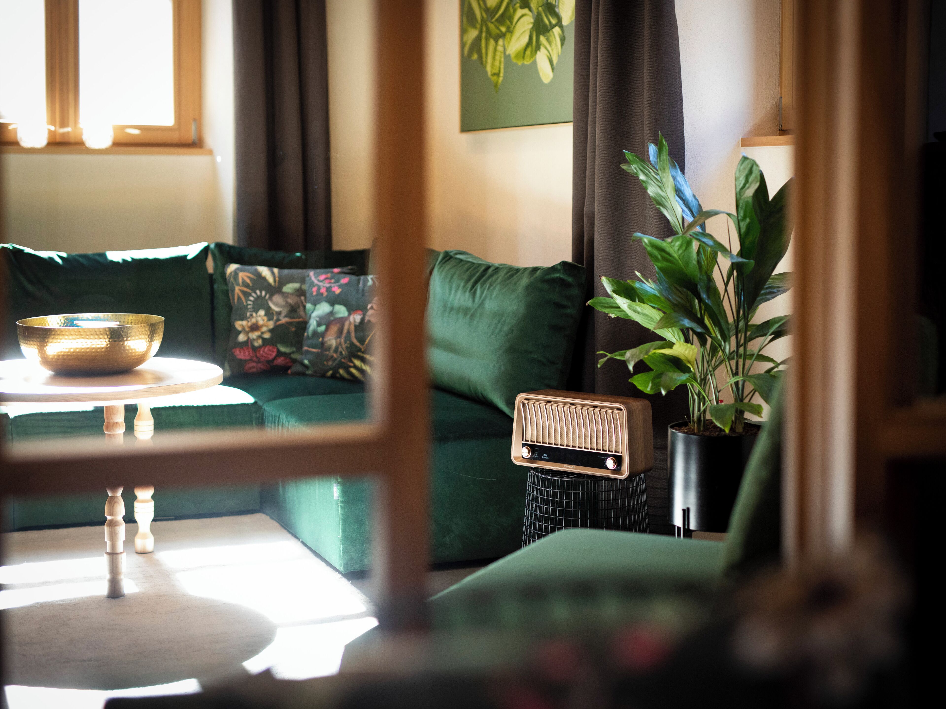 Un salon chaleureux avec un canapé vert, une petite table sur laquelle se trouve un bol, une radio ancienne et une plante en pot.
