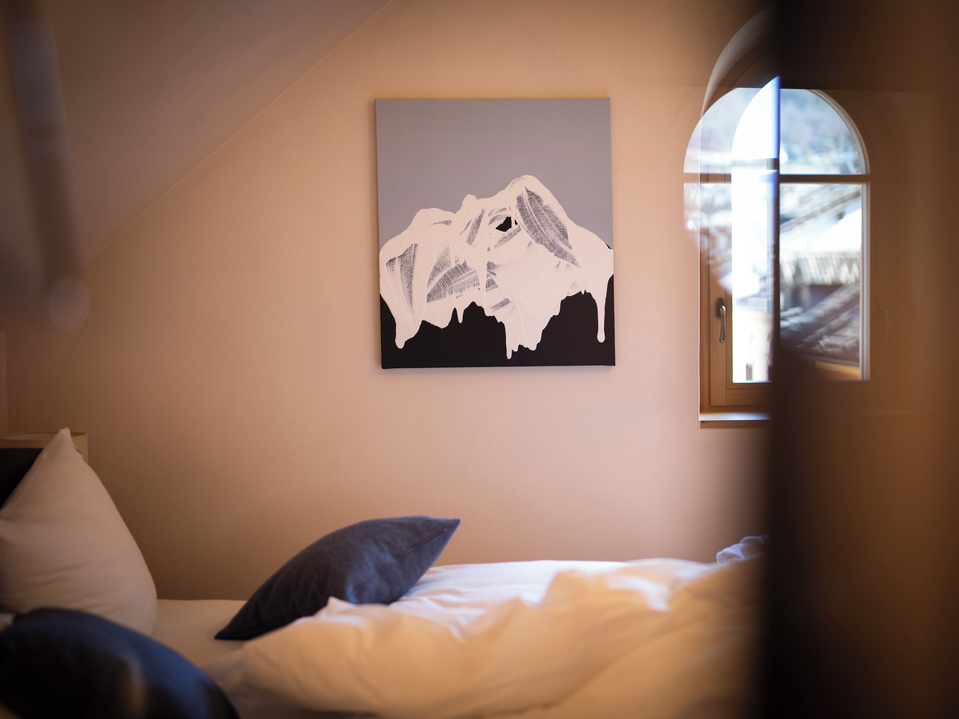 A bedroom with a bed, pillows, and a wall-mounted painting of a mountain.