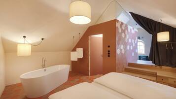 A modern bedroom with a large white bathtub, a bed with white linens, and a staircase leading to an upper level.