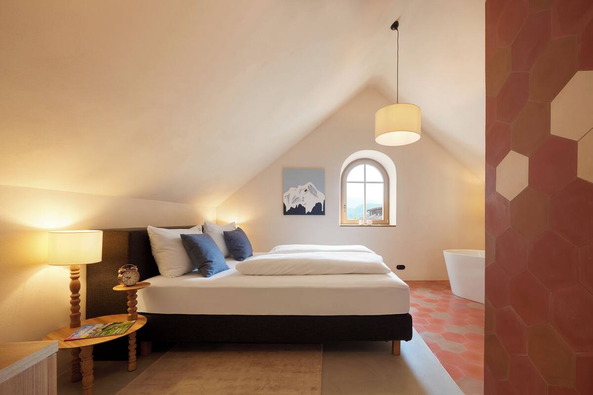 A bedroom with a bed, bedside table, lamp, and a window.