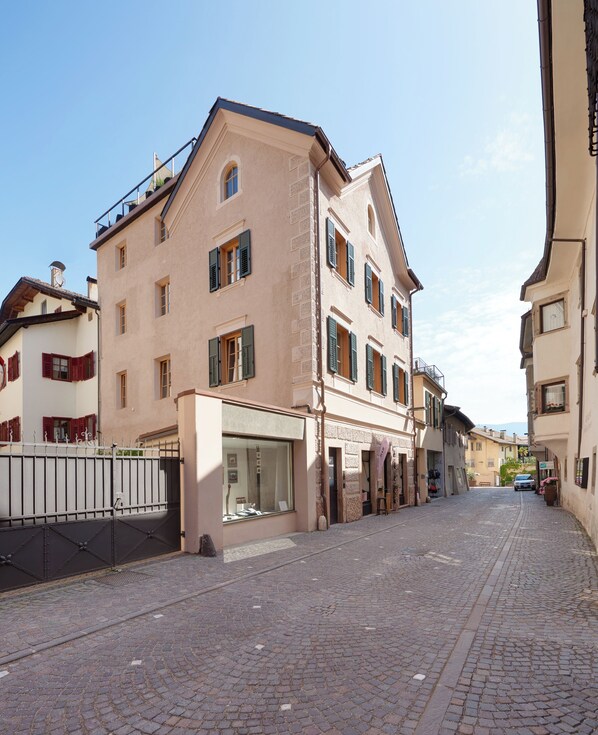 A cobblestone street lined with historic buildings, featuring a large glass storefront and a metal gate. - Goldengel Suiten im Herzen von Kaltern (Caldaro Sulla Strada del Vino)