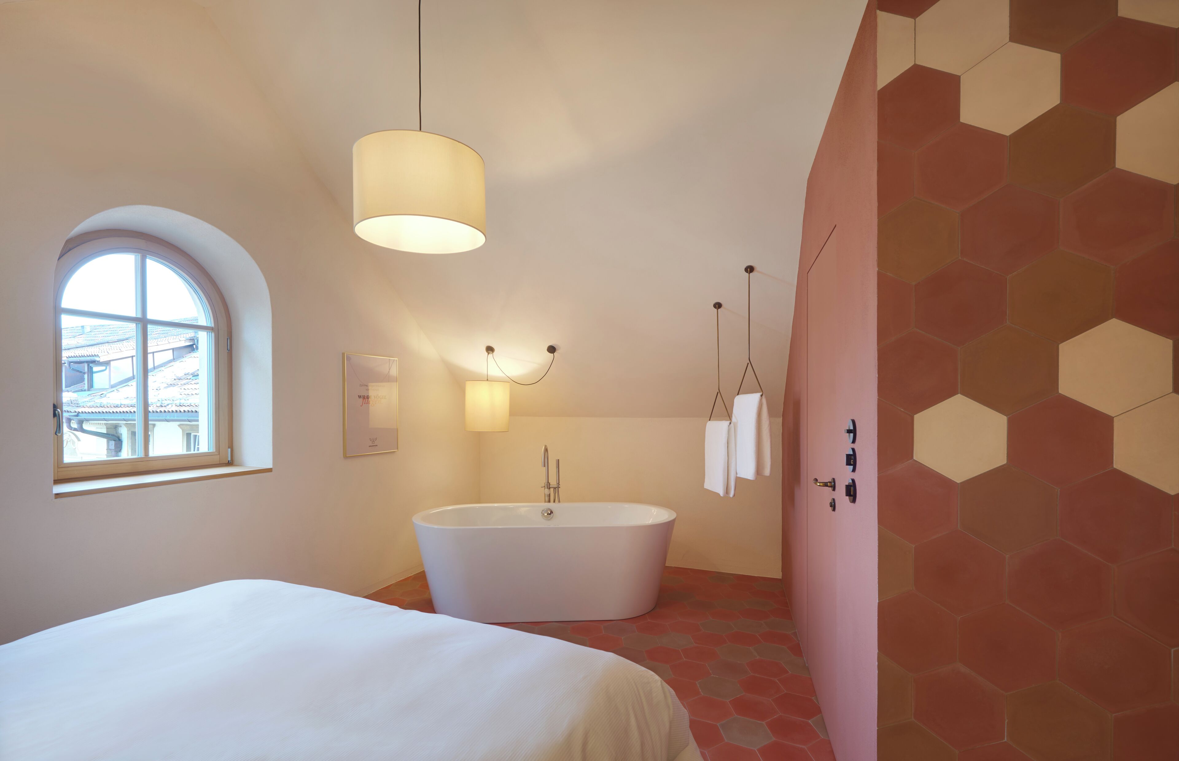 A modern bathroom with a freestanding bathtub, a large window, and a unique hexagonal tile pattern on the walls.