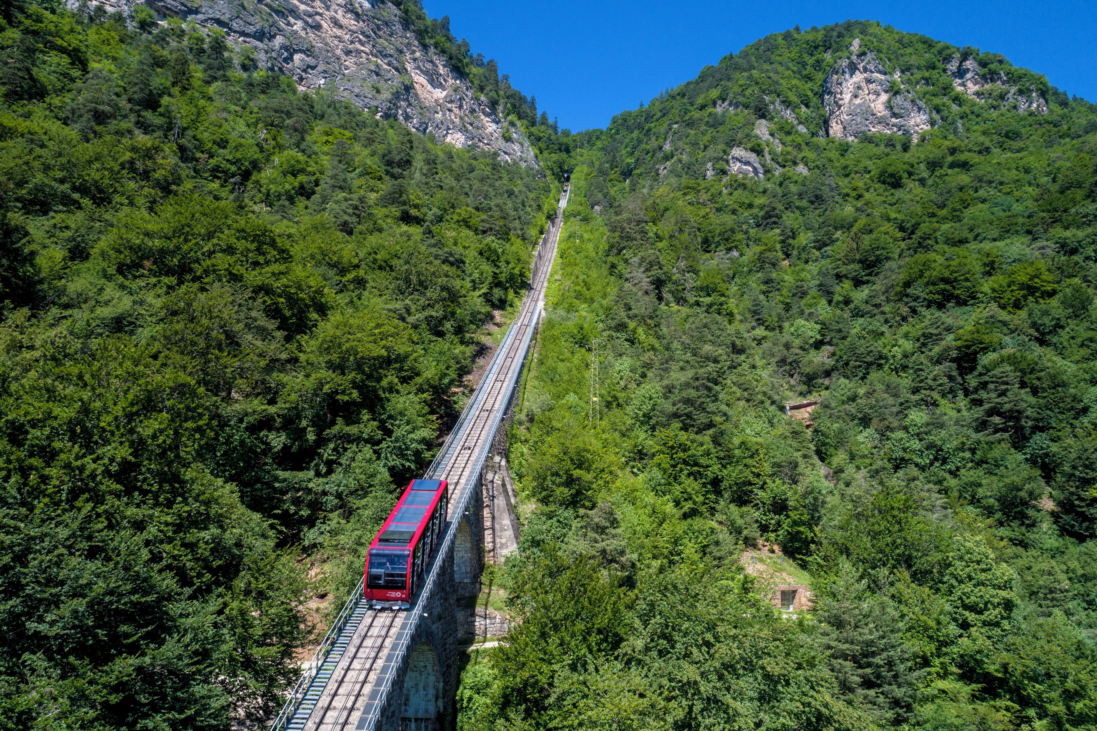 Un train rouge traverse un pont au-dessus d’une vallée boisée.