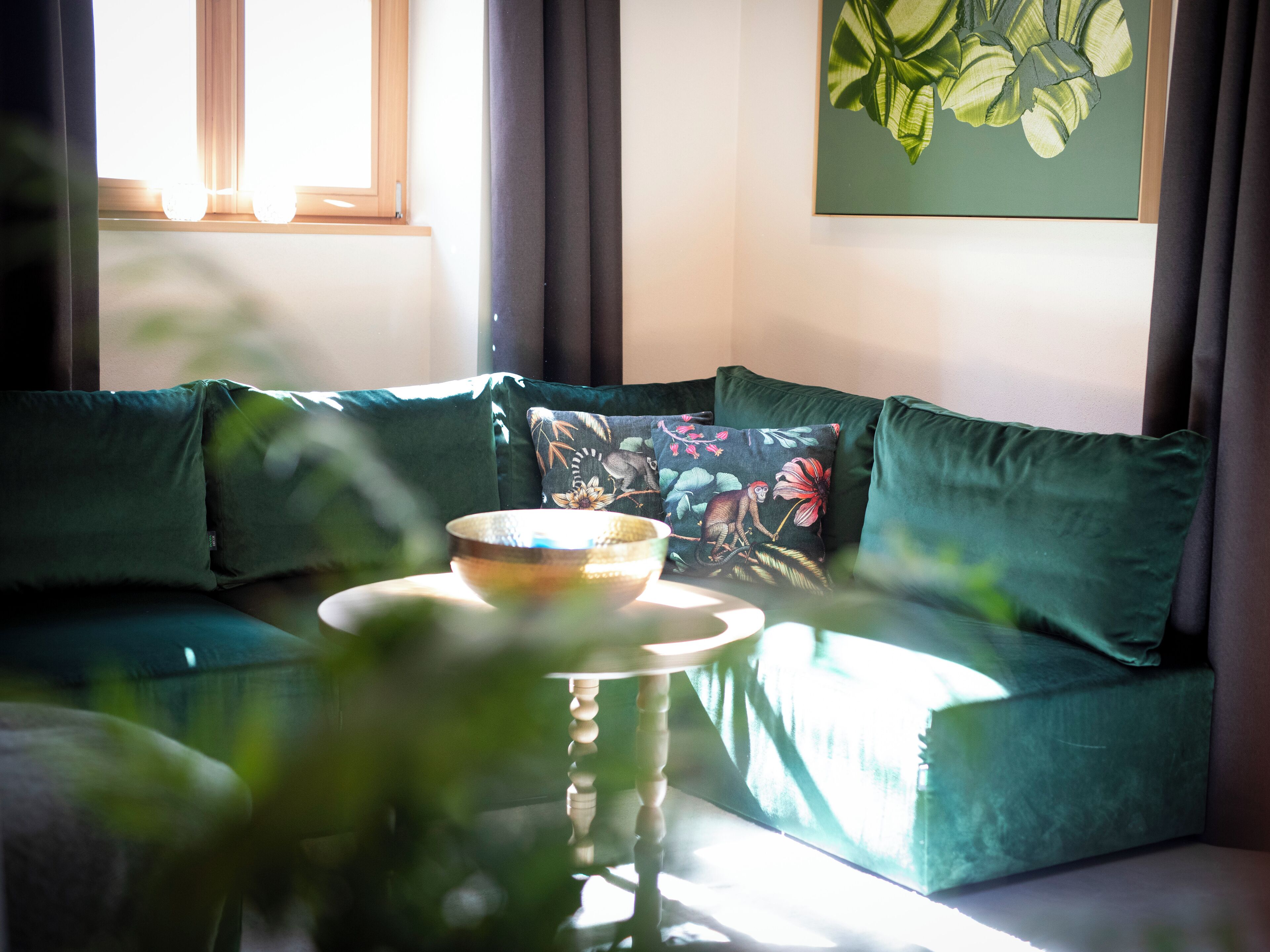 Een groene bank met bloemkussens, een schaal op een tafel en een schilderij aan de muur.