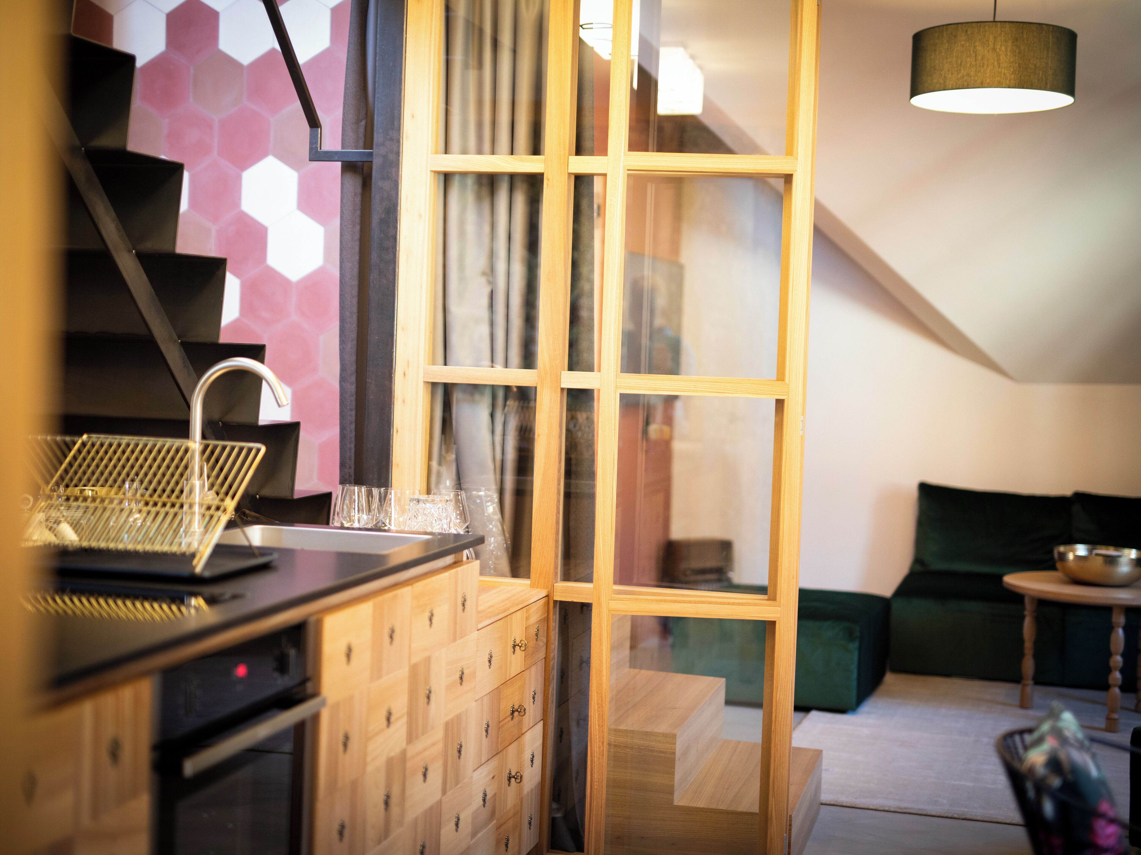 A modern kitchen with a built-in stove, a sink, and a glass dish rack. There is a wooden cabinet with multiple drawers and a window with a view of the outside.