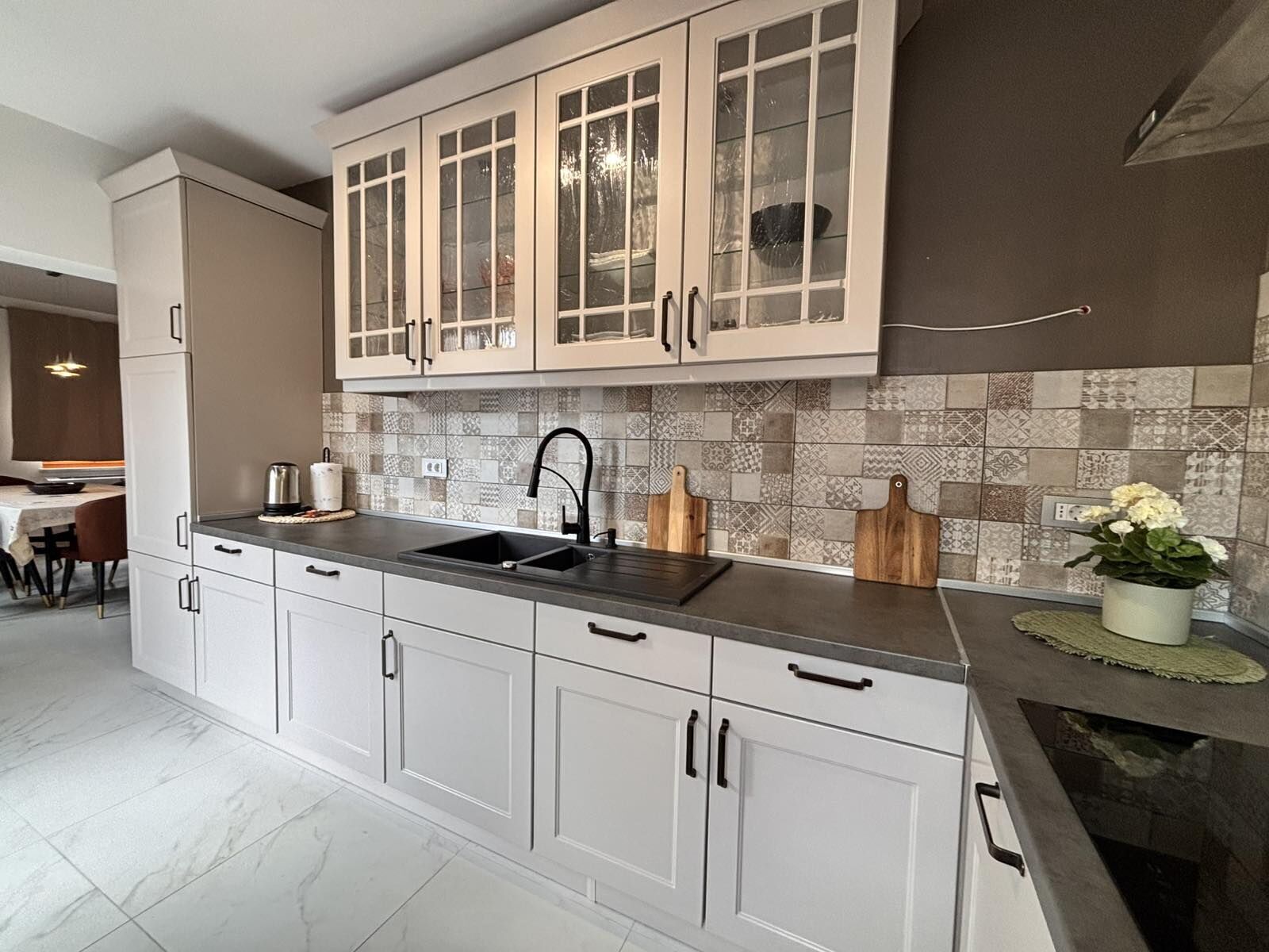 A modern kitchen with white cabinets, a black countertop, and a tiled backsplash.