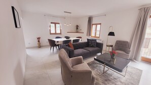Ett modernt vardagsrum med en grå soffa, ett soffbord och en matplats med ett vitt bord och stolar.