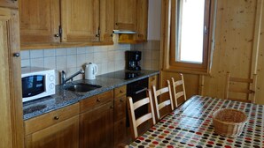 Une cuisine avec des meubles en bois, un four à micro-ondes, une machine à café et une table à manger recouverte d’une nappe à pois.