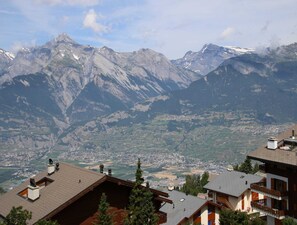 Un village de montagne aux maisons traditionnelles en bois, une vallée et, au loin, des sommets enneigés.